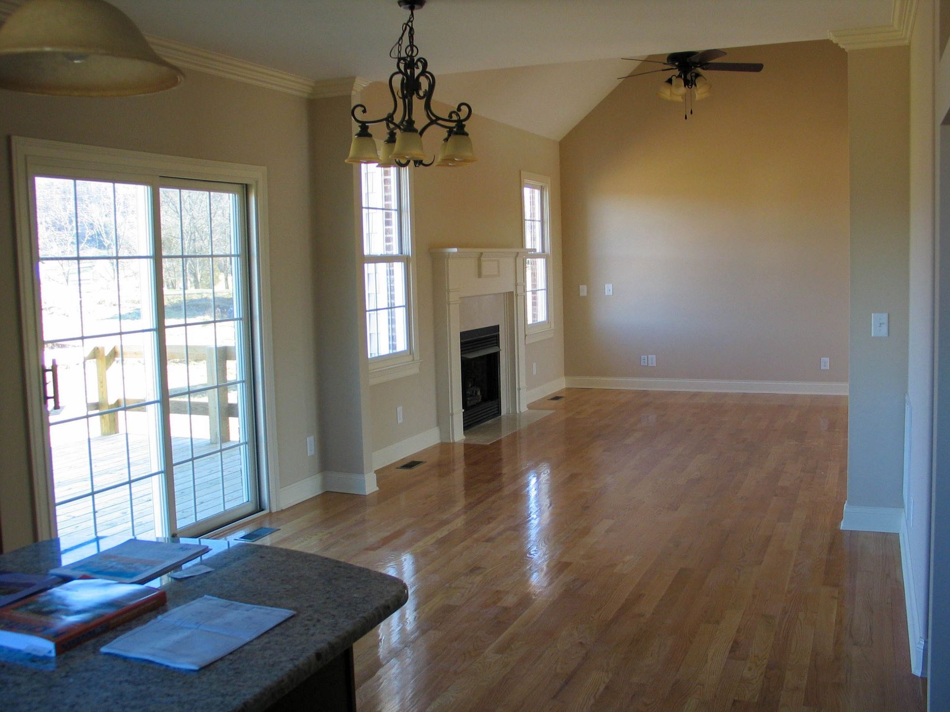 Empty living room with hardwood floors, fireplace, chandelier, and sliding glass doors to a deck