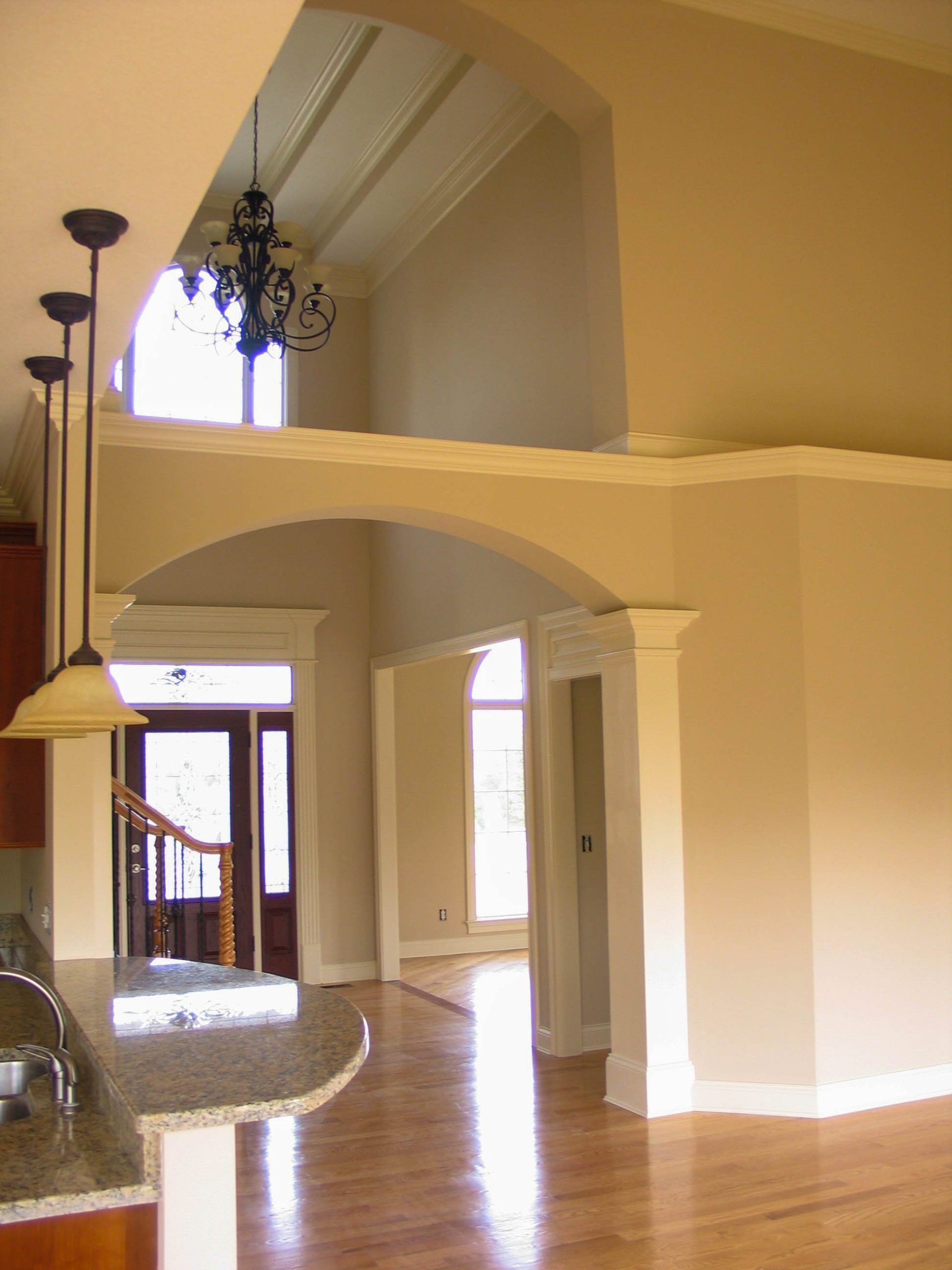 Spacious beige foyer with arched openings, high ceiling, chandelier, and polished wood floor.