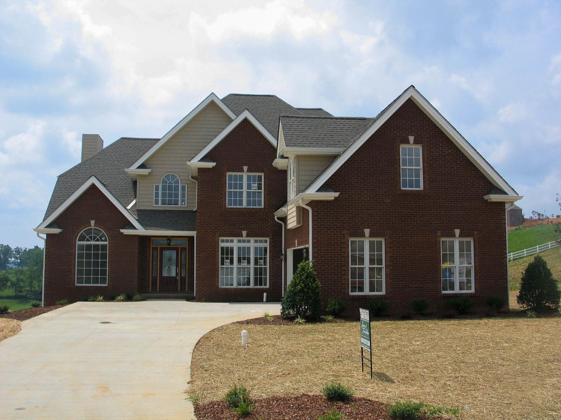 Large two-story brick house with a gray roof, front driveway, and landscaped yard