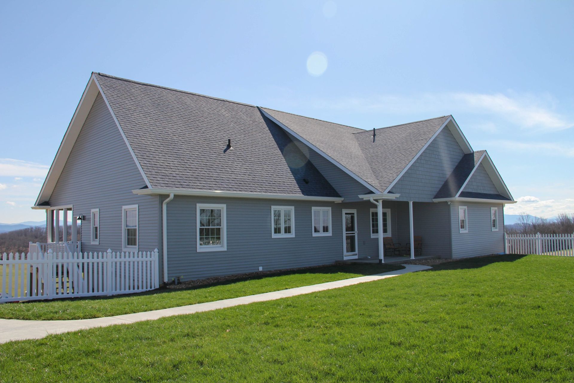 Gray house with a large sloped roof and white fence on a green lawn under a clear sky