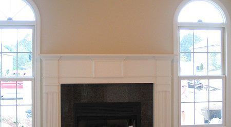 White fireplace with tall arched windows and beige walls in a bright room.