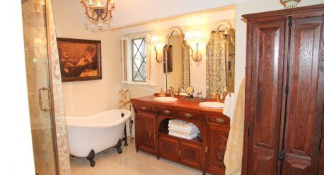 Elegant bathroom with a clawfoot tub, ornate wooden vanity, mirror, sconces, and dark wood cabinet
