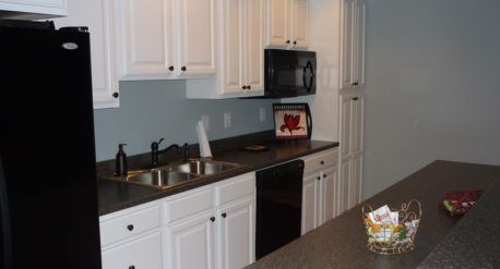 Modern kitchen with white cabinets, black appliances, dark countertops, and a bowl on the island.