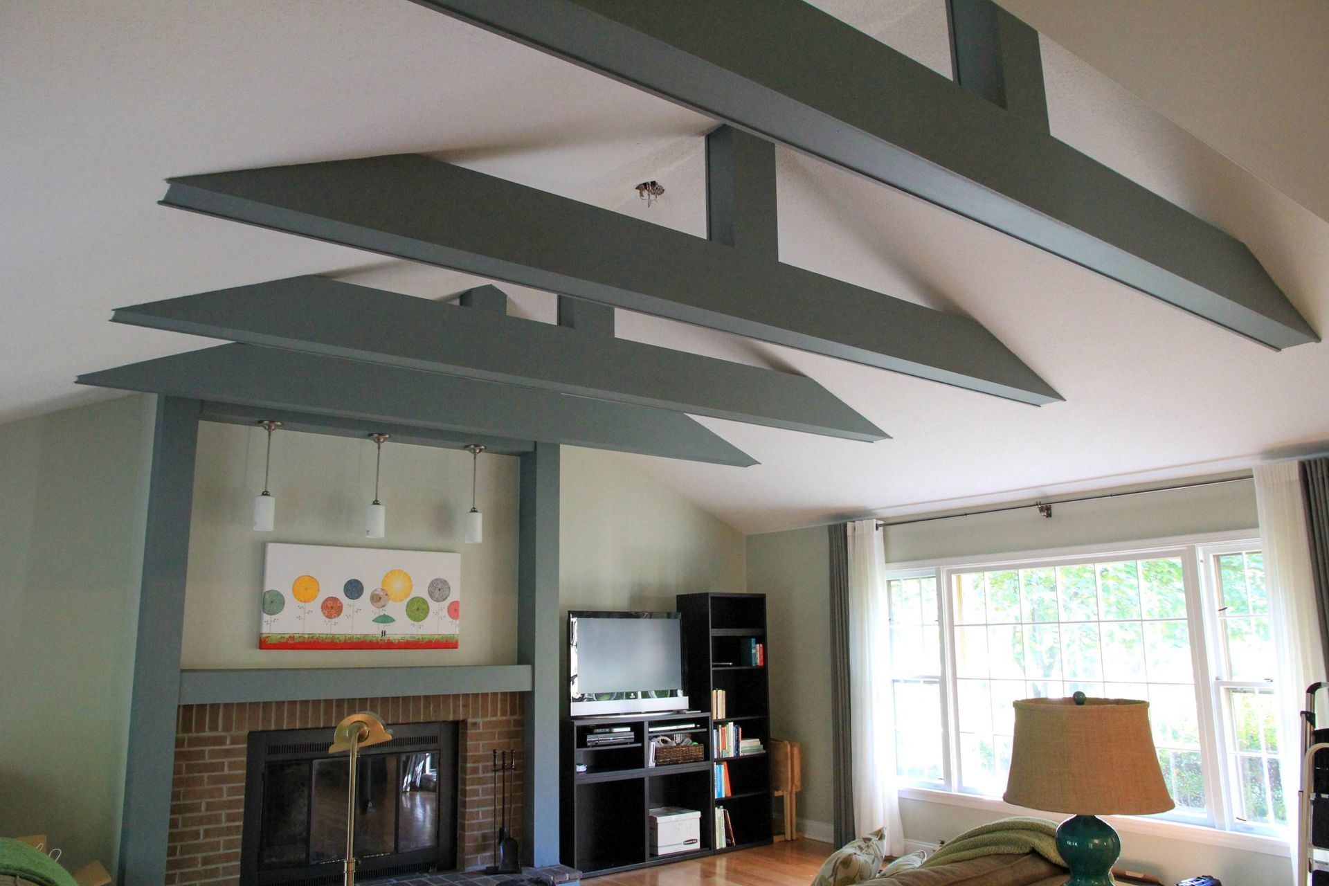 Living room with angled ceiling beams, fireplace, TV, and large windows overlooking a bright patio