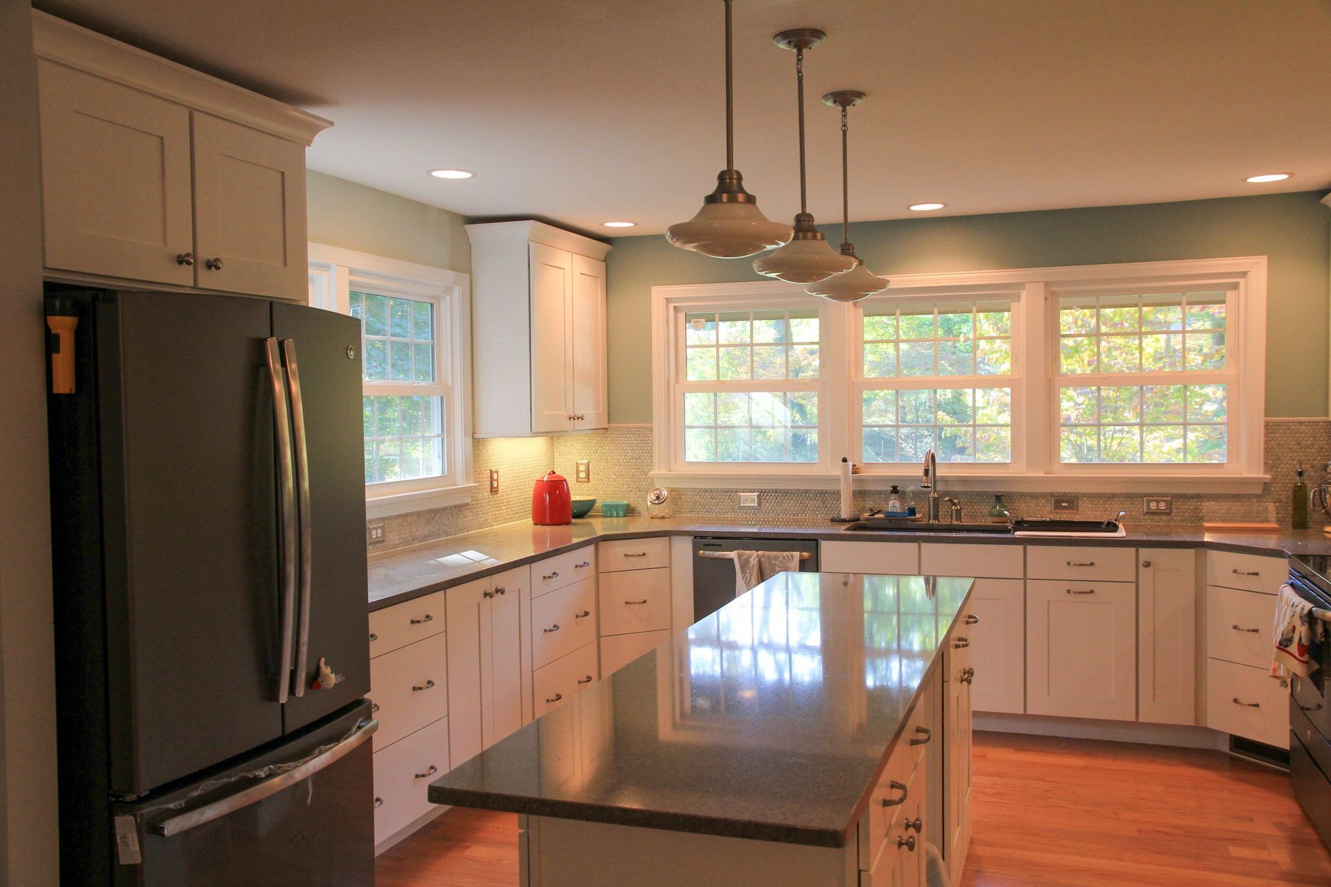 Bright, modern kitchen with a large island, white cabinets, black refrigerator, and big windows.