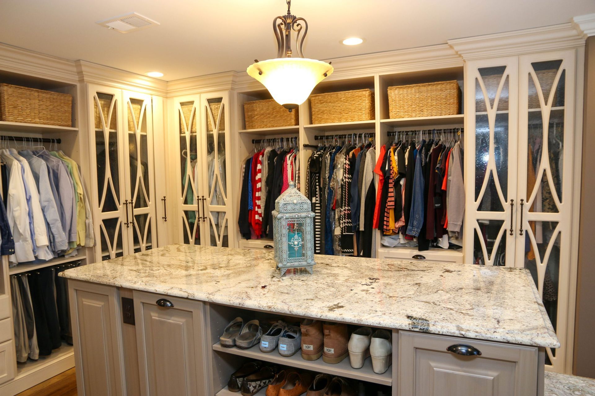 Walk-in closet with open hanging clothes, shelves, and a large marble island under warm lights