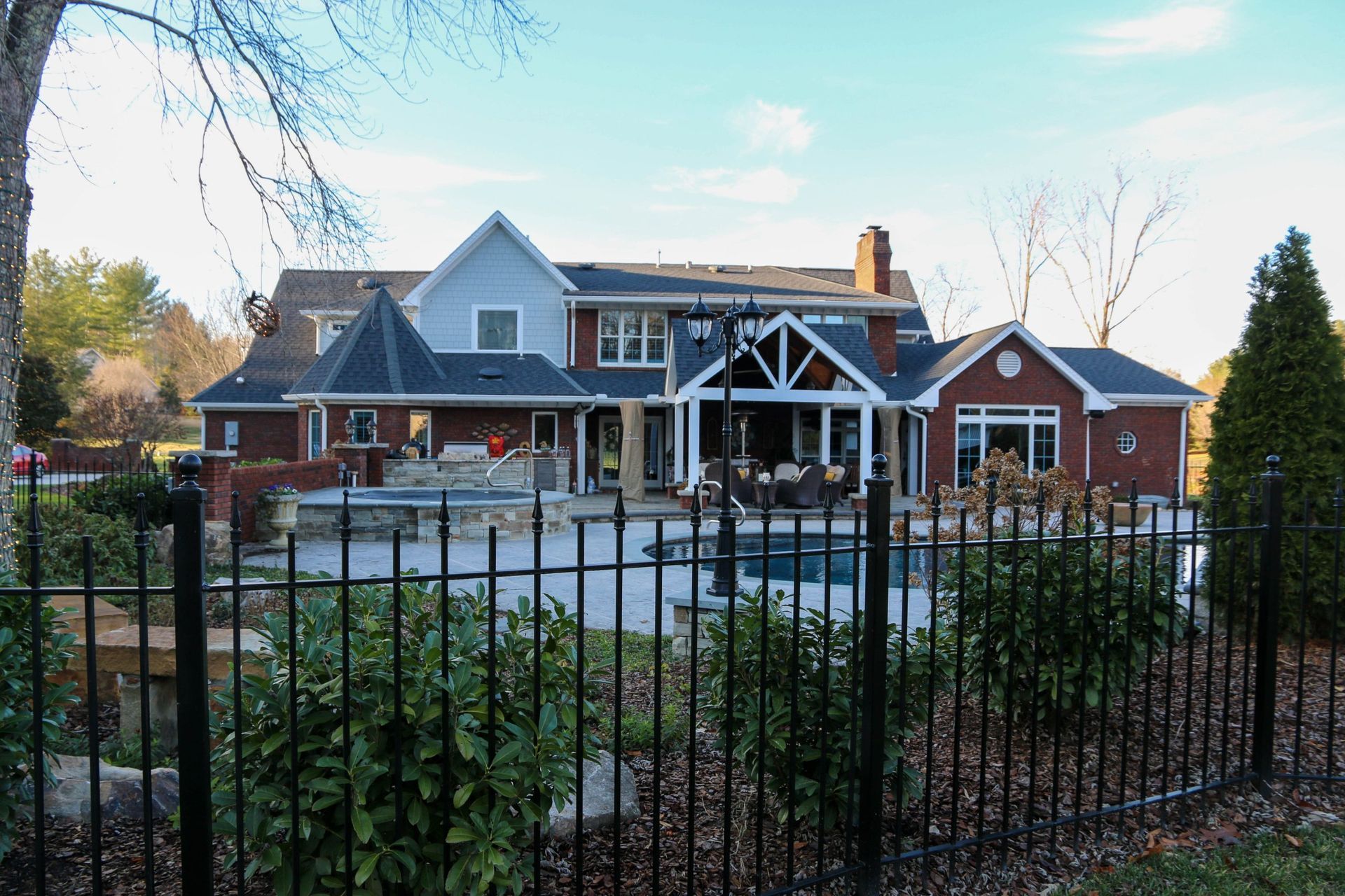 Large brick house with a gabled roof behind a black metal fence and landscaped yard