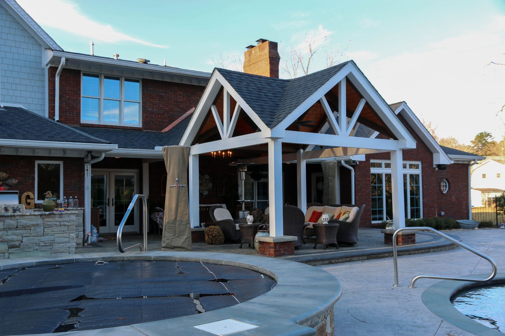Backyard patio with white wooden pergola, brick house, and swimming pool under construction