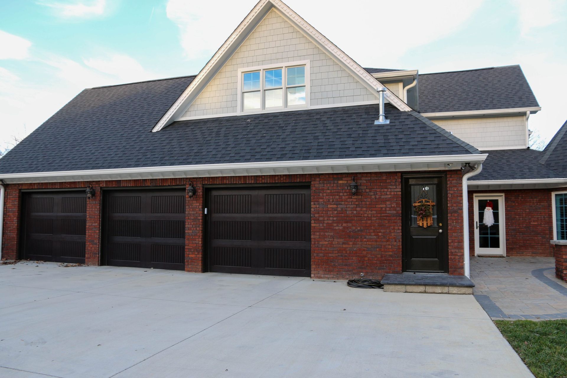 Brick suburban house with three dark garage doors and a white gabled roof under construction