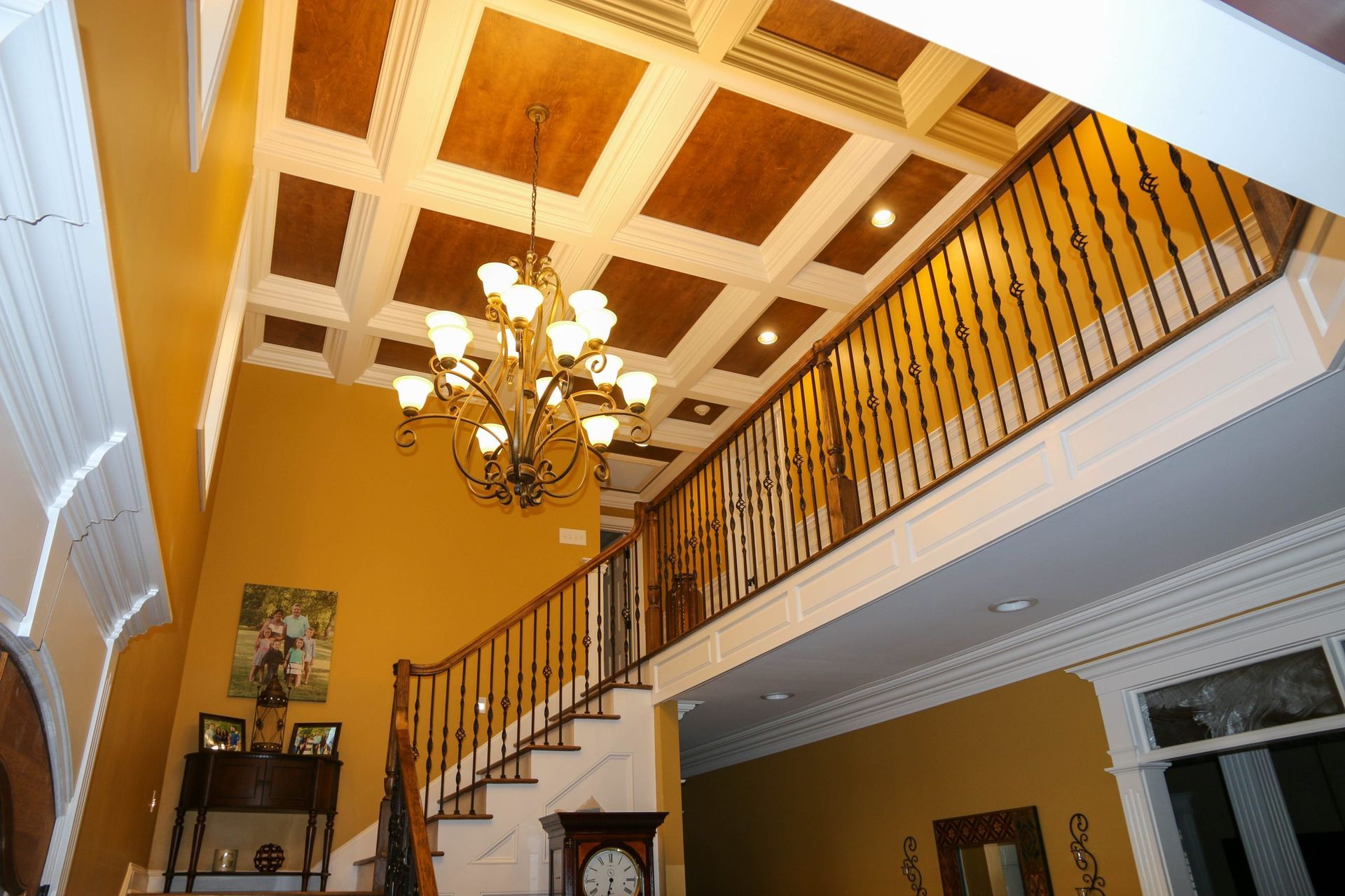 Grand foyer with a staircase, chandelier, and coffered ceiling in warm yellow tones