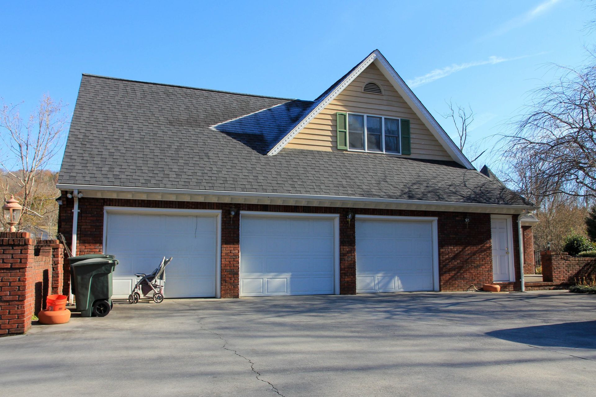 Brick house with three garage doors and a steep roof under a clear blue sky