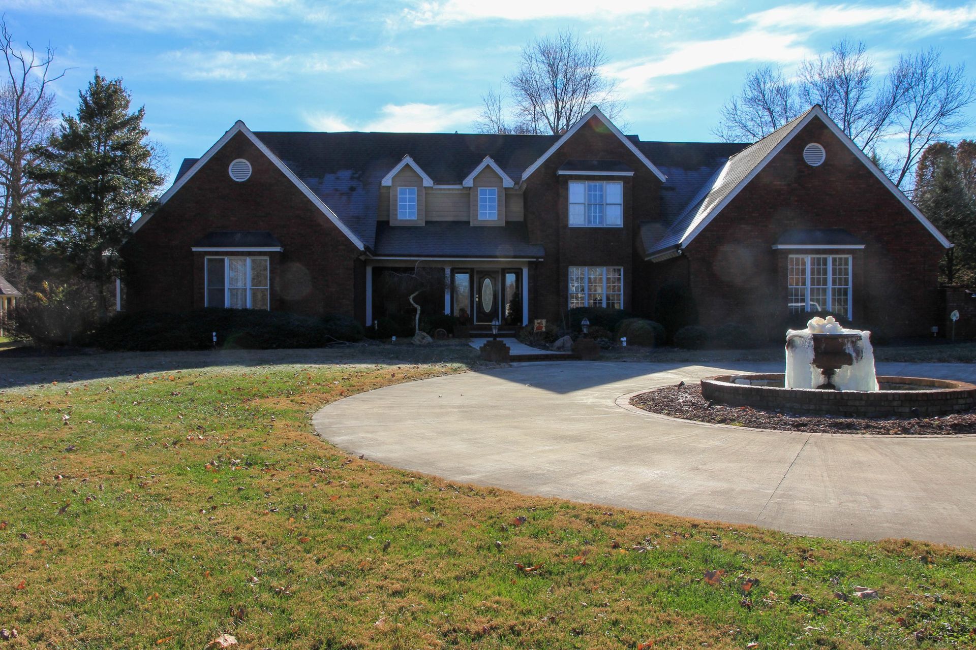 Large brick suburban house with a circular driveway and a fountain in the front yard