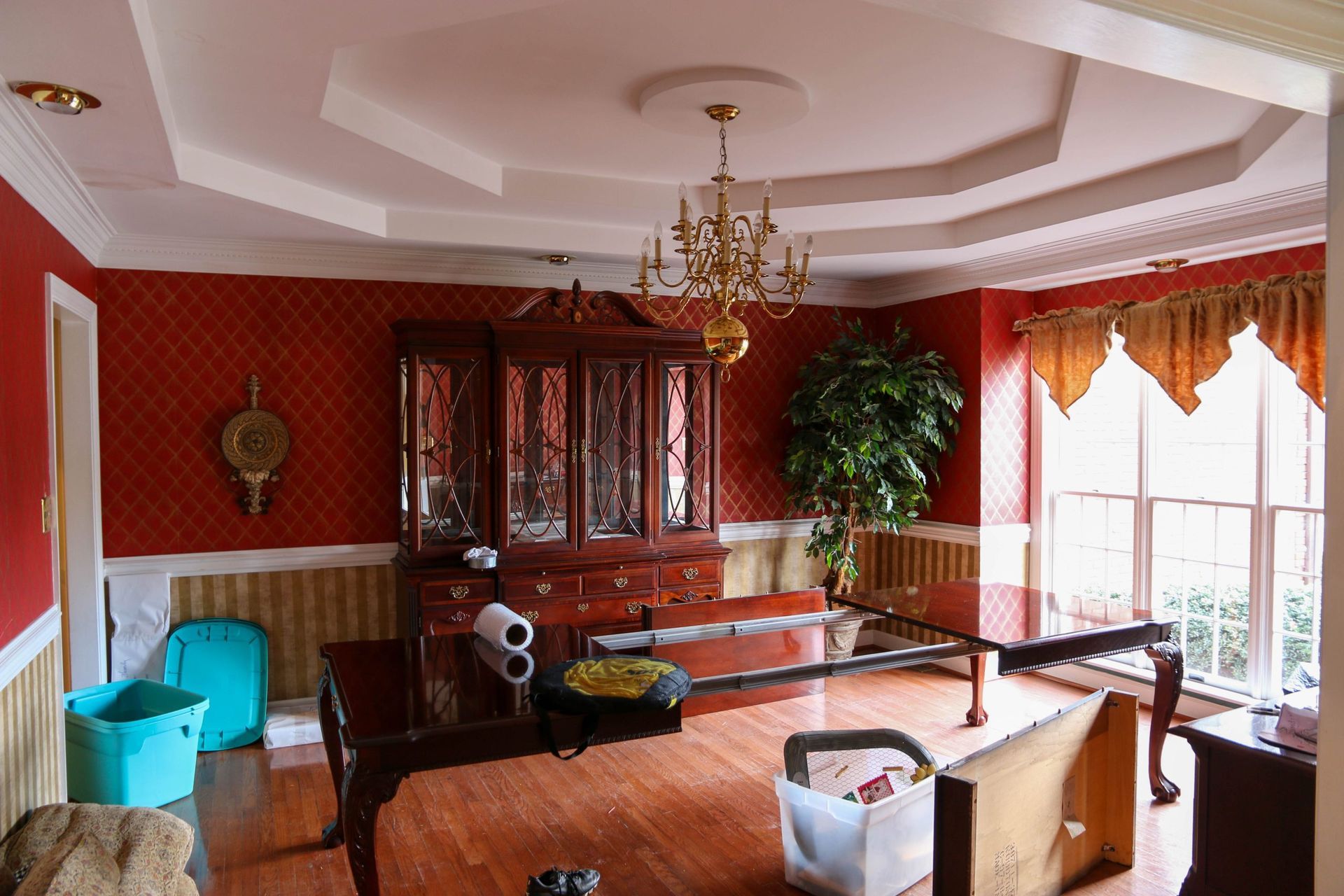 Elegant living room with red walls, chandelier, wood furniture, and large windows with drapes