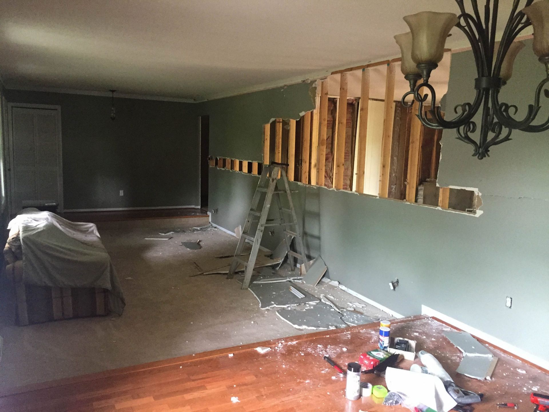 Partially demolished living room with exposed studs, debris, and a ladder against the wall.