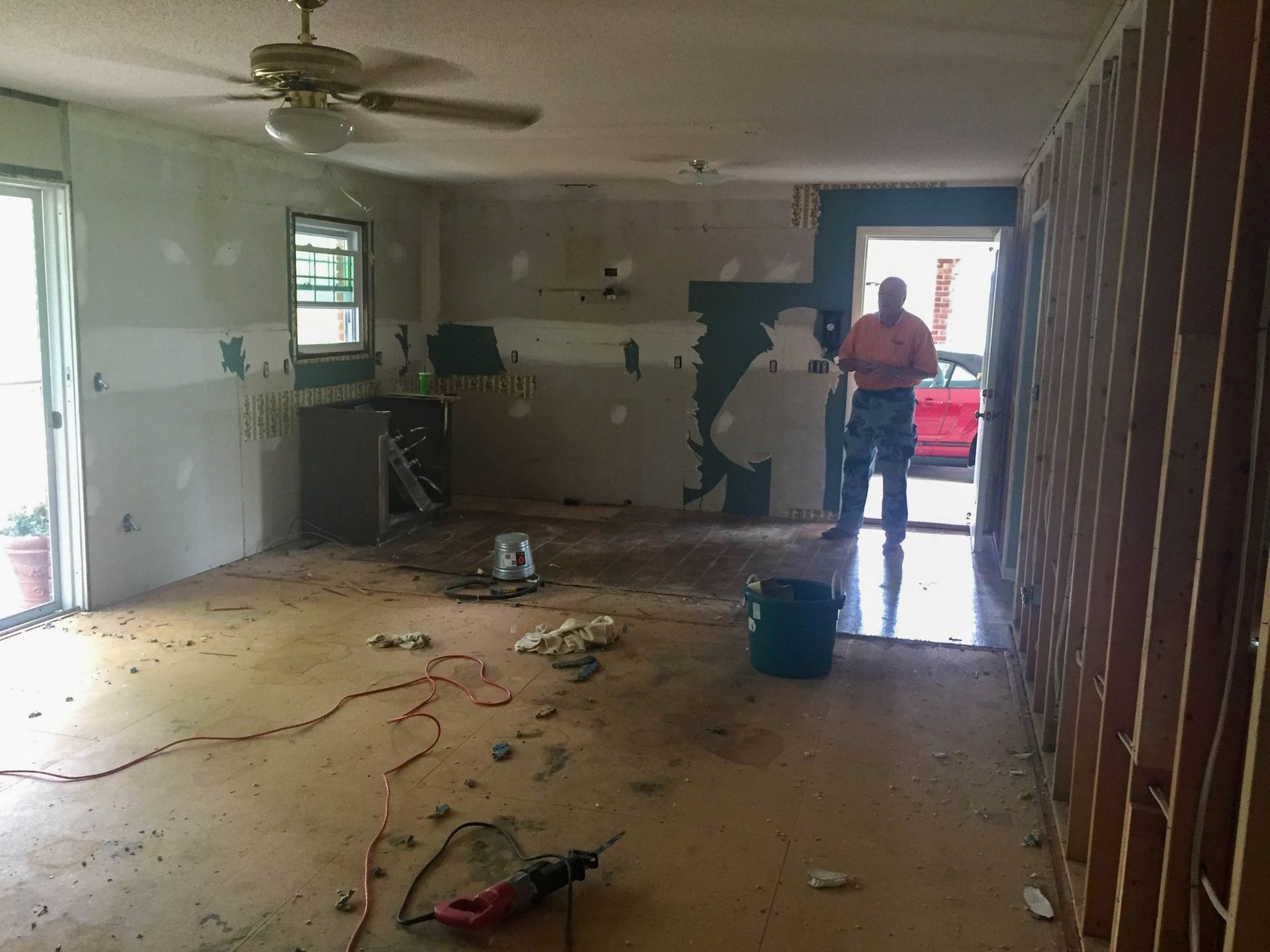 Damaged room with debris on the floor and a person standing by the doorway.