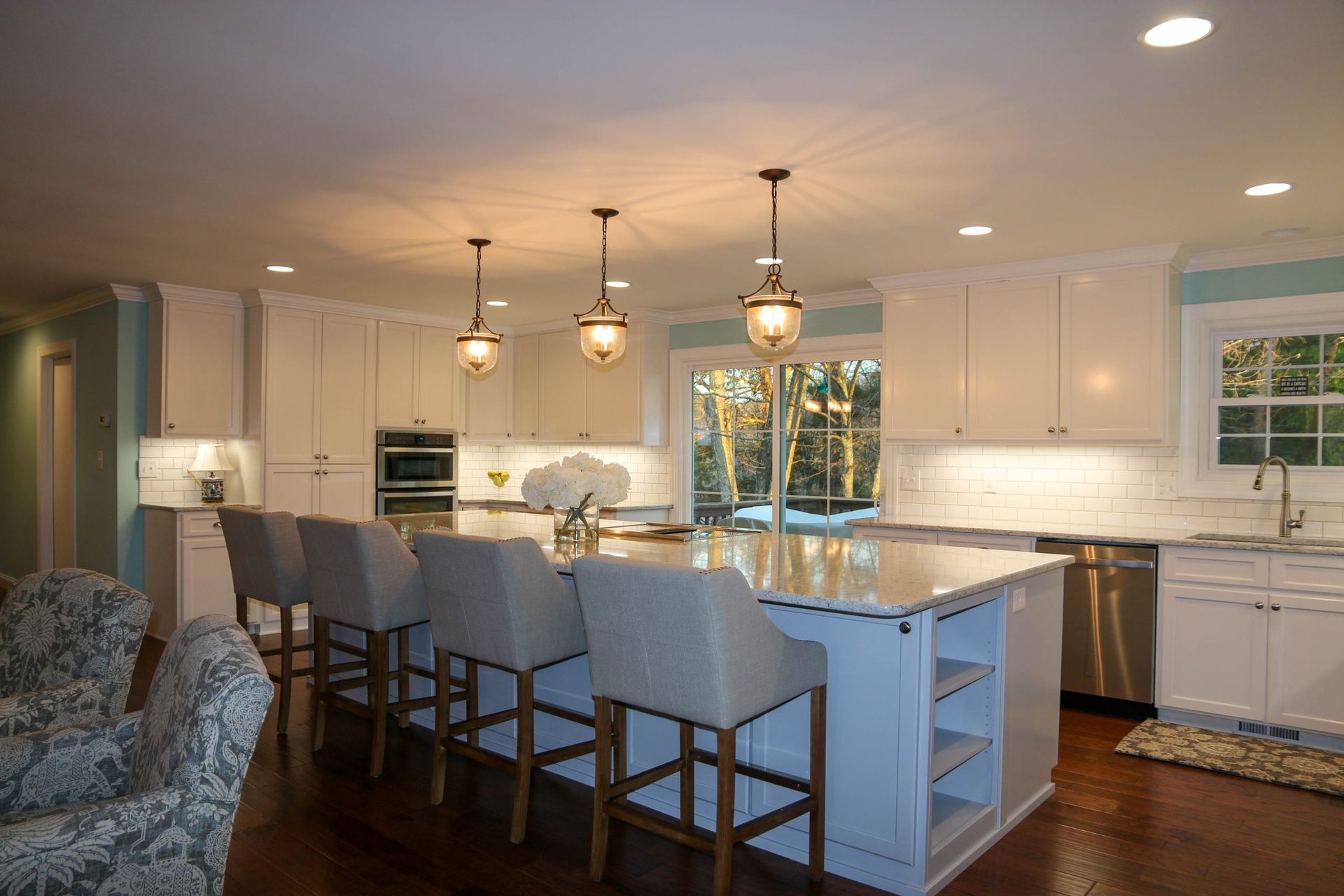 Bright modern kitchen with white cabinets, island seating, pendant lights, and large windows