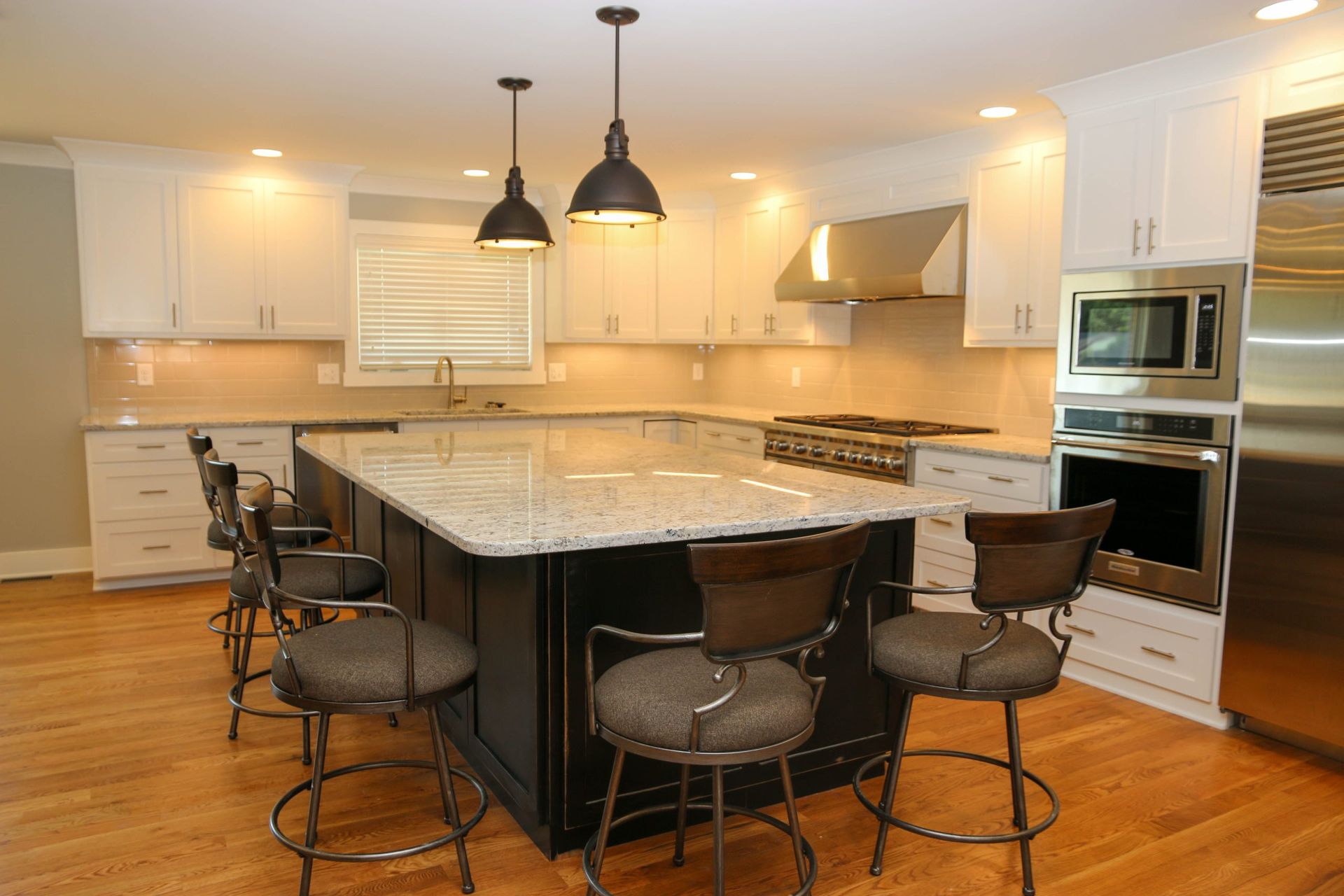 Bright modern kitchen with large island, white cabinets, stainless appliances, and black barstools.