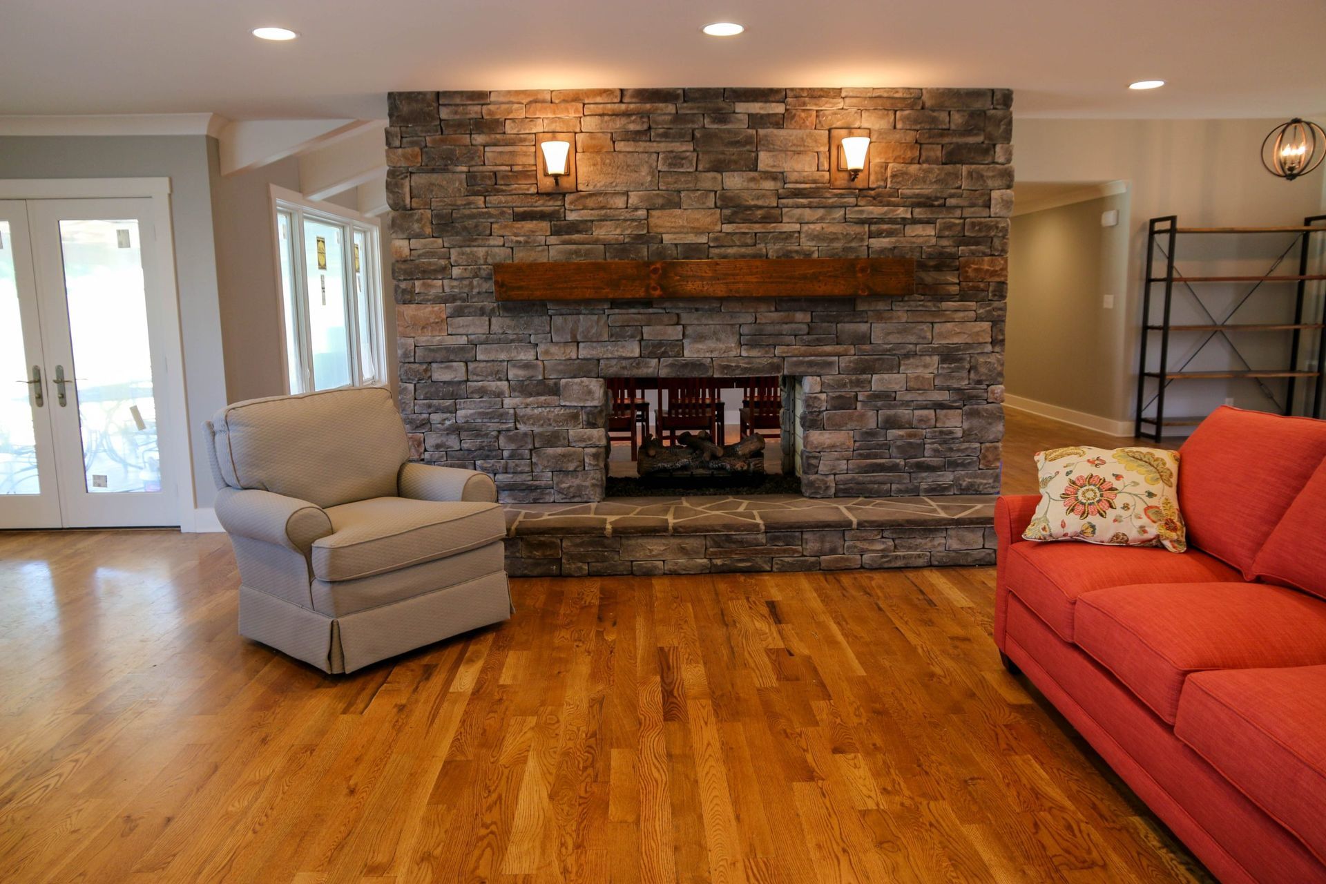 Living room with stone fireplace, red sofa, gray chair, and hardwood floors