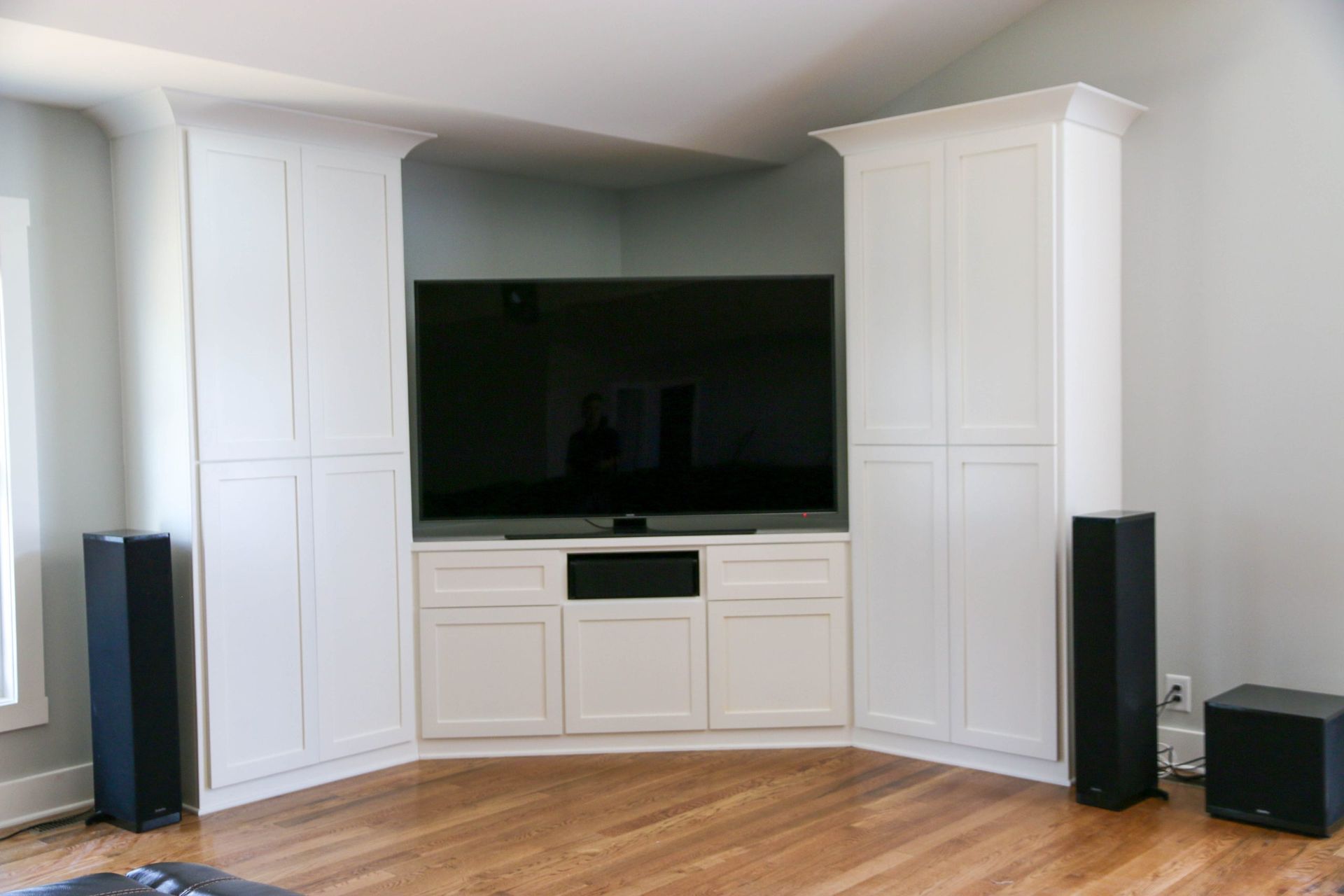 Built-in entertainment center with large TV, white cabinets, and speakers in a bright living room