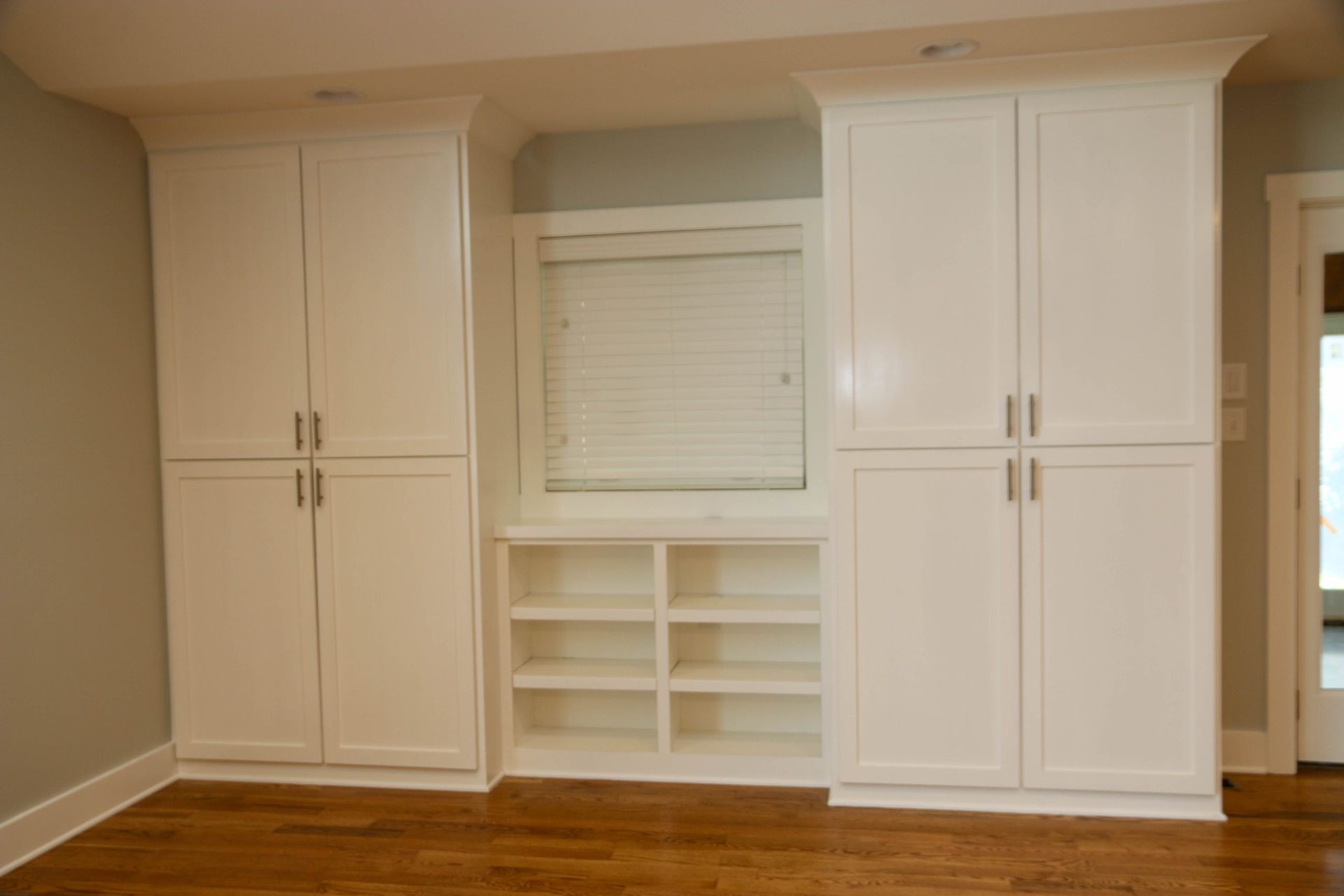 Built-in white cabinets and shelves around a window seat in a beige room with hardwood floors
