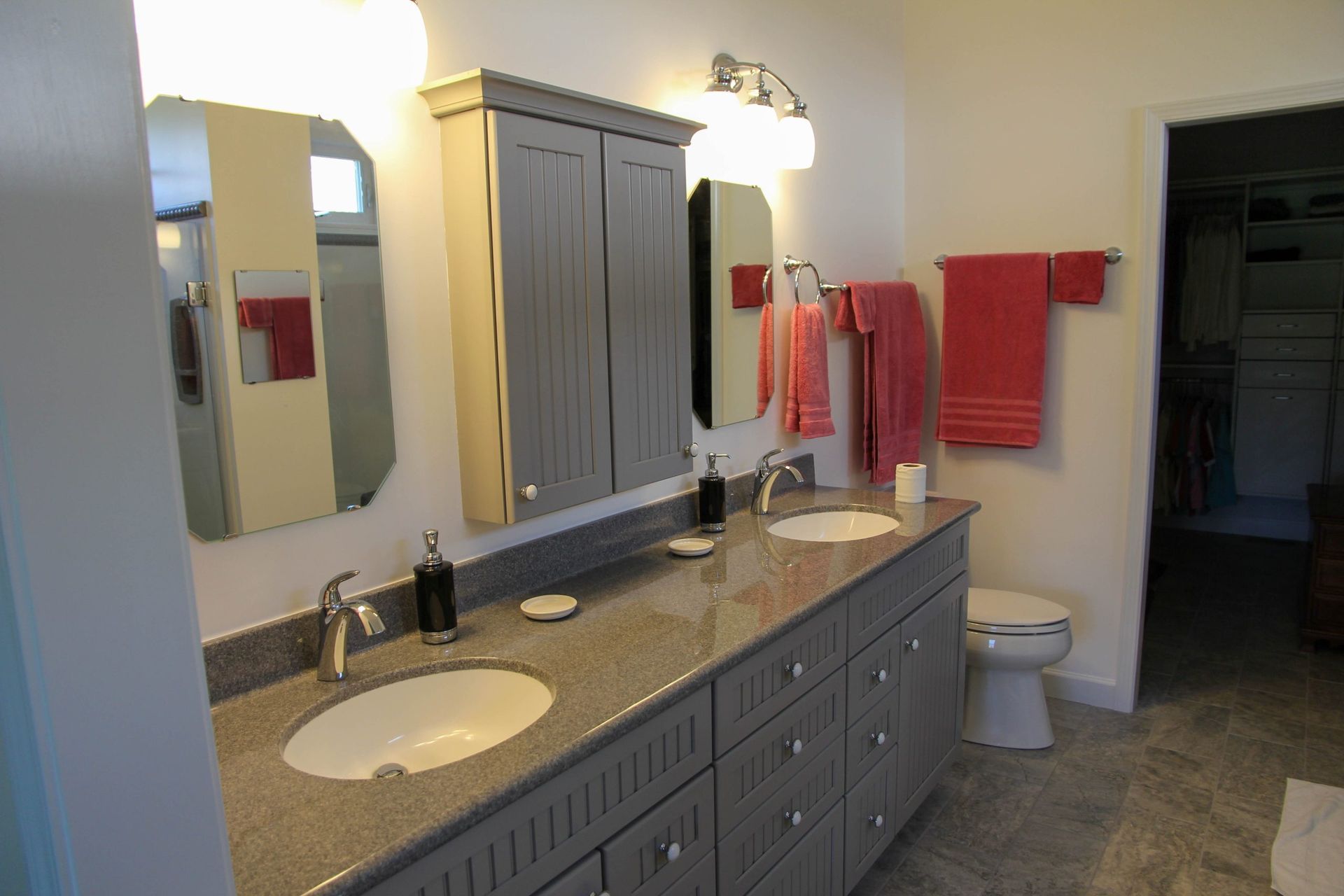 Bathroom vanity with two sinks, large mirror, gray cabinets, and red towels on the wall.