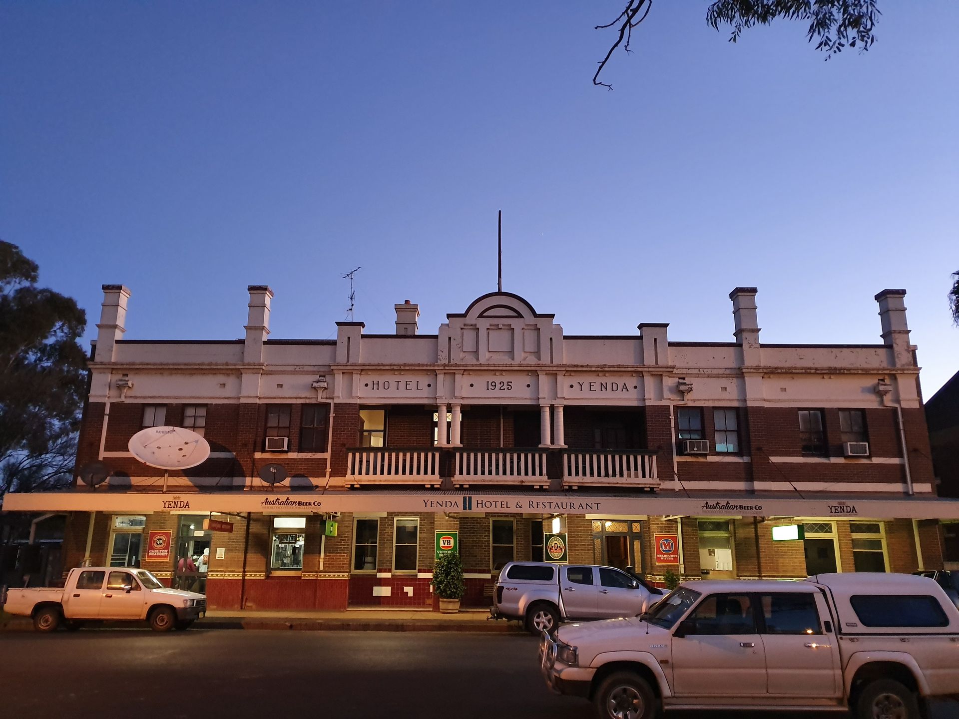 Historic two-story brick hotel at dusk with parked cars and lit storefronts below