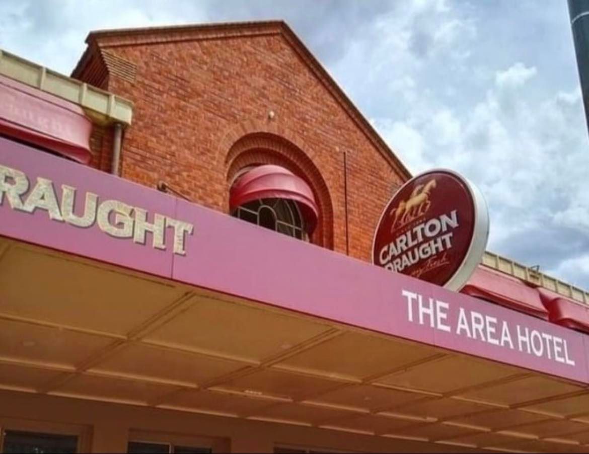 Carlton Draught signage on a pink awning beside a brick building labeled “The Area Hotel.”