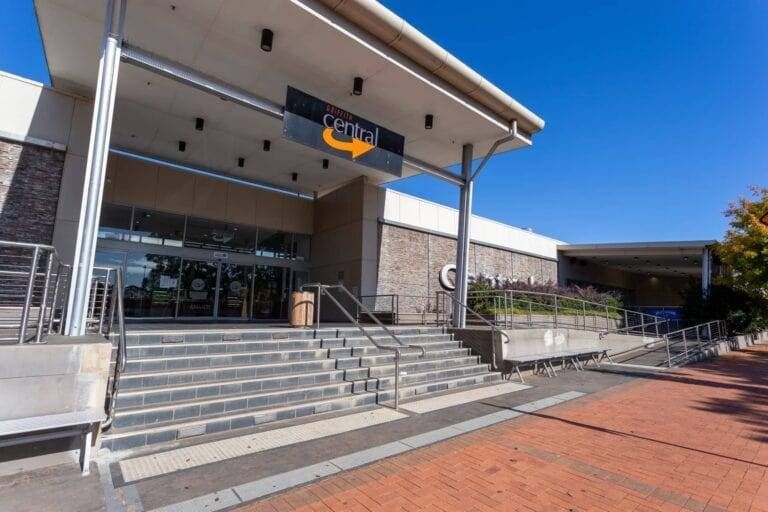 Civic building entrance with wide steps, ramps, glass doors, and red brick walkway under a clear blue sky
