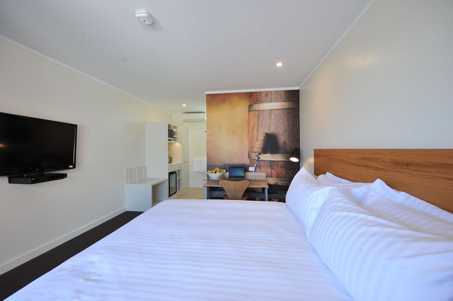 Modern hotel room with white bed, wall-mounted TV, and large window seat area
