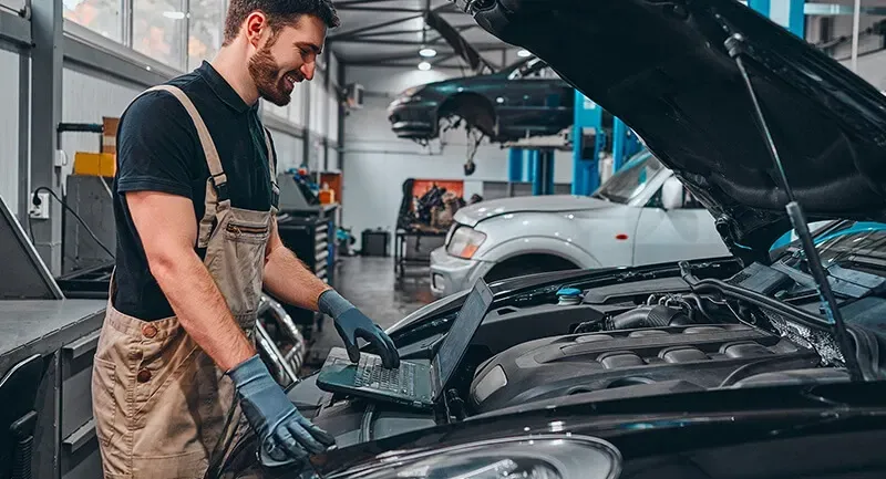 Mechanic in overalls uses a laptop to diagnose a car engine in a garage | Calgary Auto and Alignment