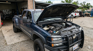 Dark blue pickup truck with hood open, parked outside an auto shop