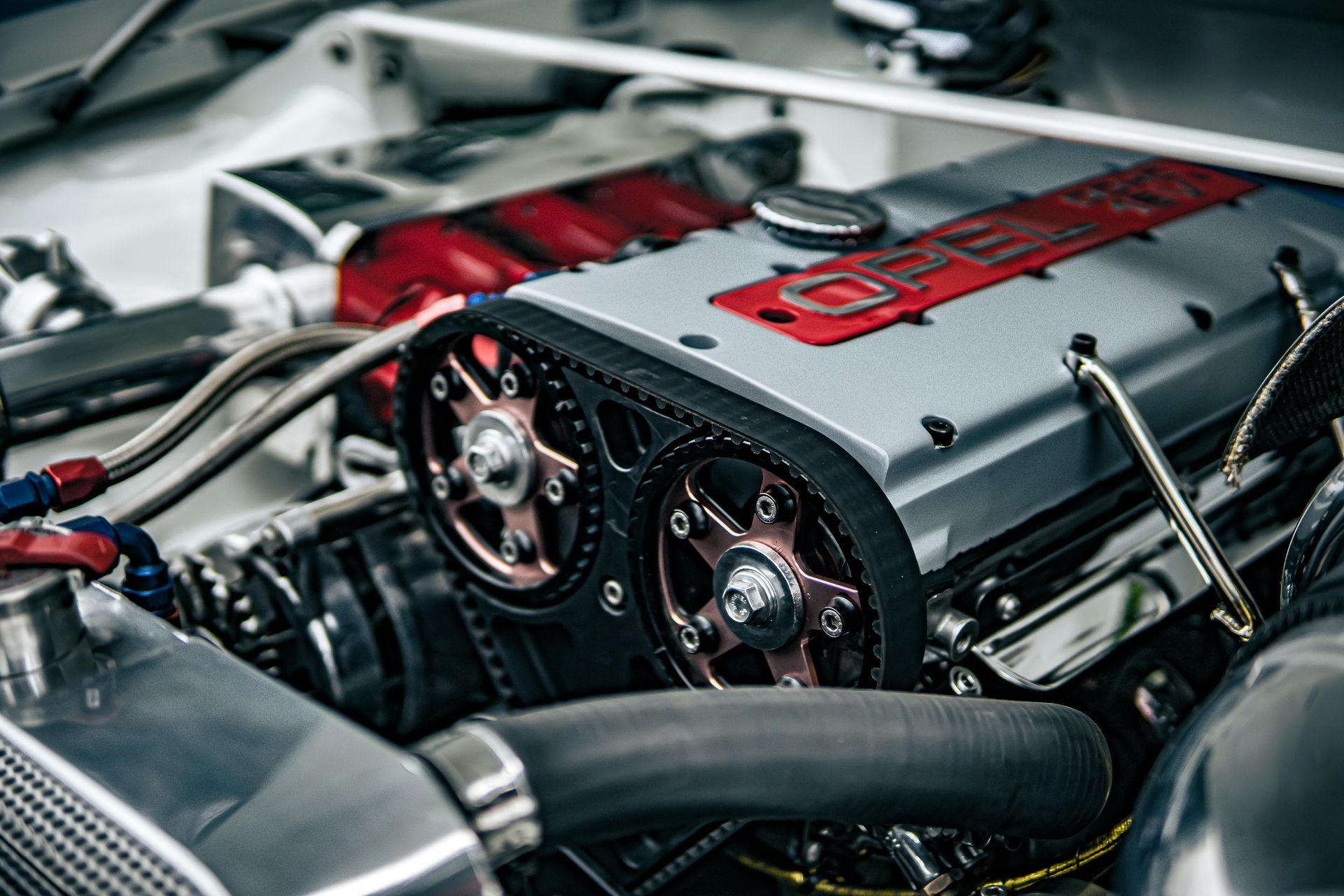 Close-up of a modified car engine with silver valve cover, red accents, and exposed pulleys in a bay