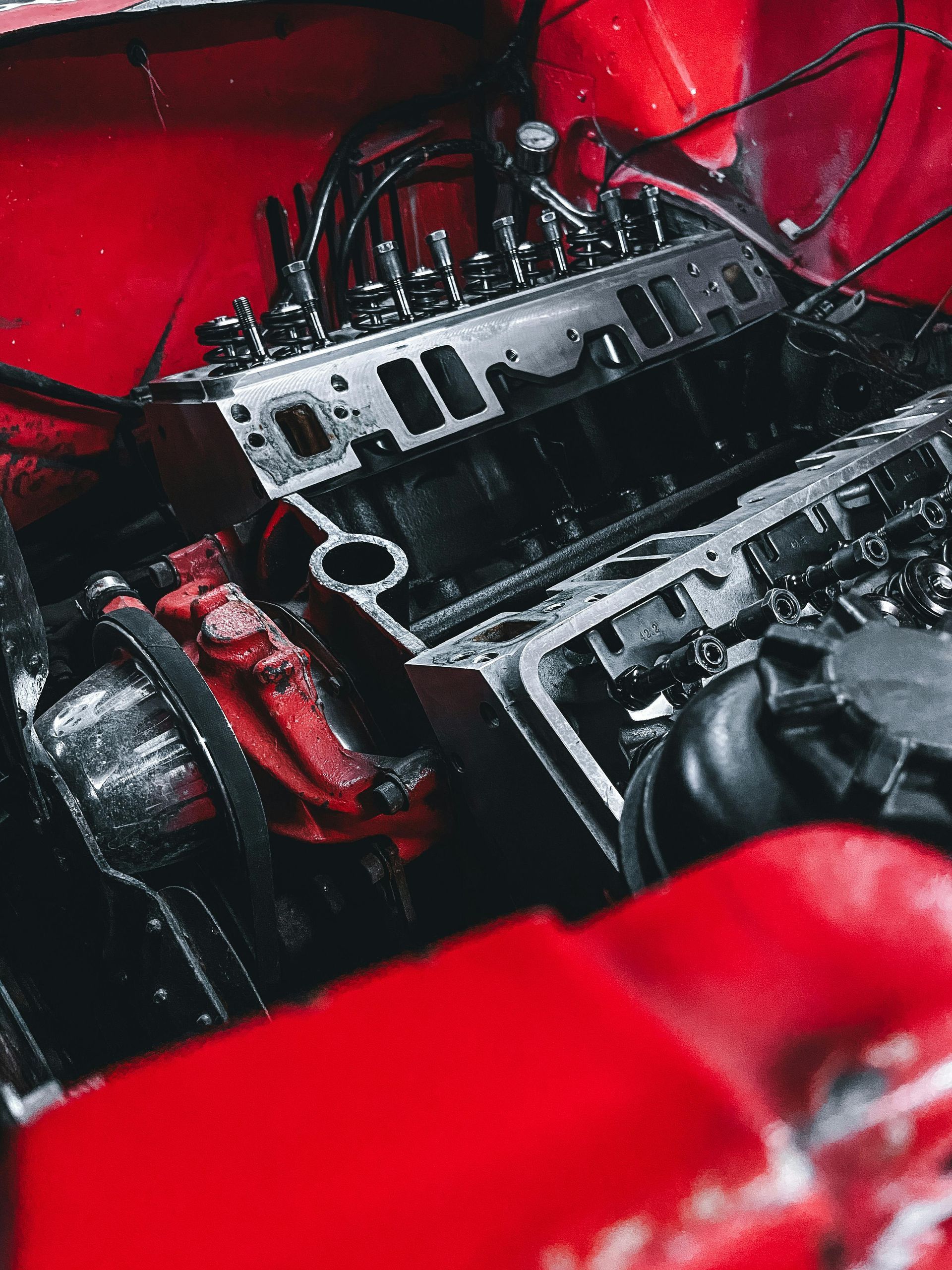 Close-up of a red car engine bay with exposed black engine components and hoses