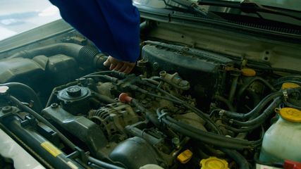 Open car engine bay with a person’s blue-sleeved arm inspecting components