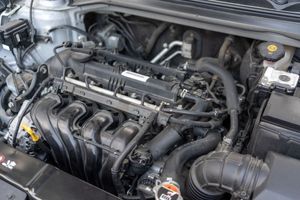 Open car hood showing a gray engine bay with hoses, battery, and engine components