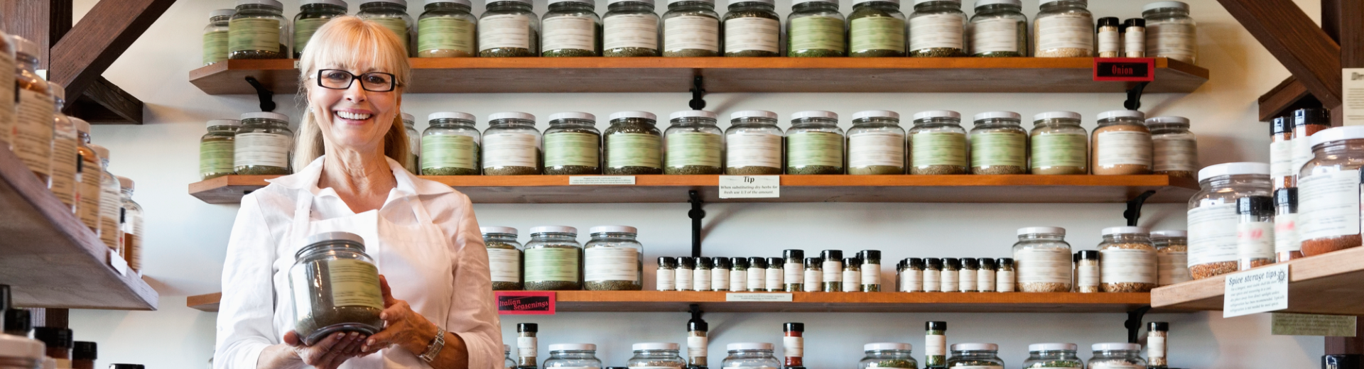 A woman is standing in front of a shelf full of jars.