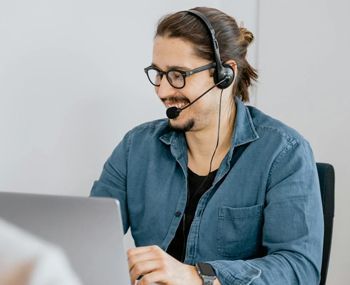 A man wearing headphones and glasses is sitting in front of a laptop computer.
