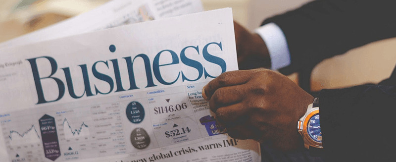 A man is reading a newspaper with the word business on it.