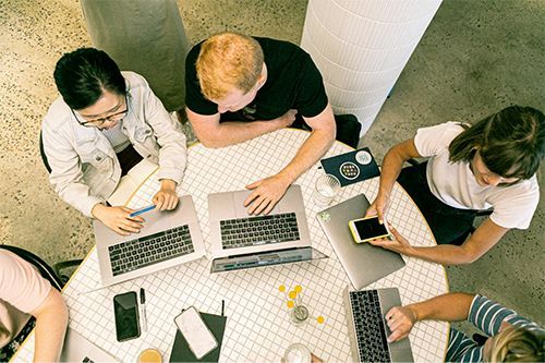 A group of people are sitting around a table with laptops.