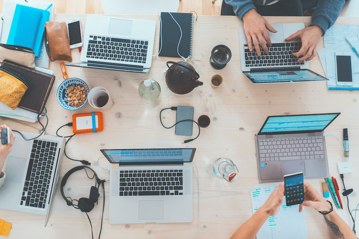 A group of people are sitting at a table with laptops and phones.