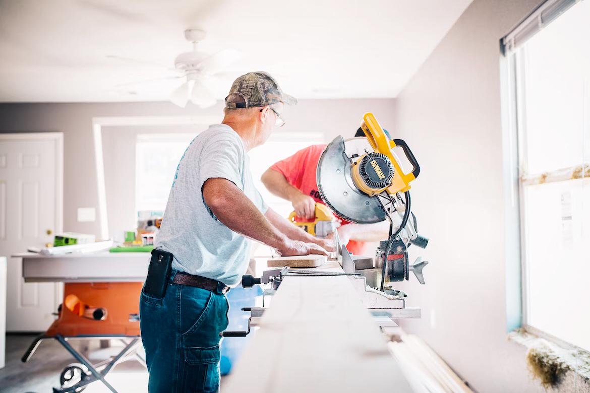 Two men are working on a circular saw in a room.