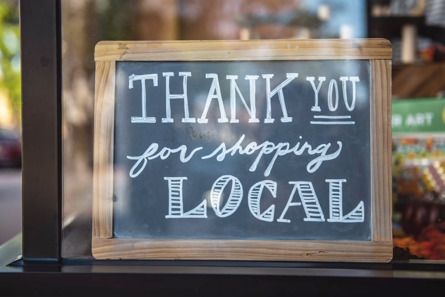 A chalkboard in a window that says `` thank you for shopping local ''.