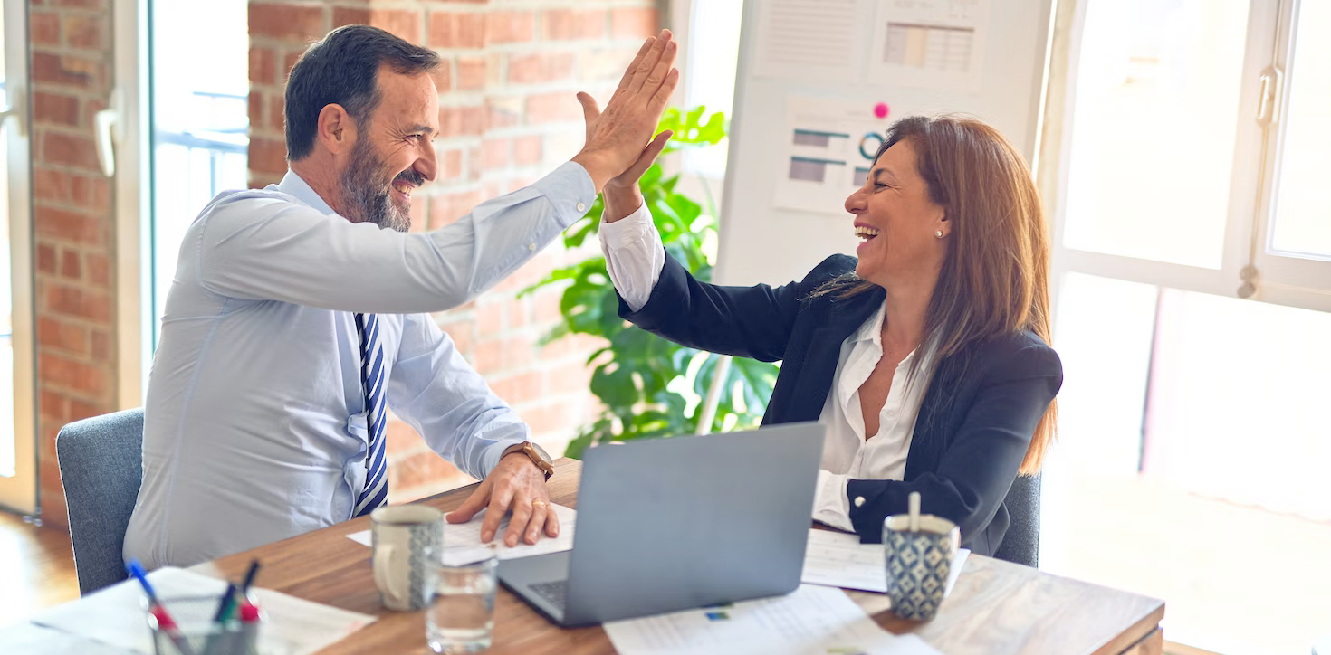 a man and a woman are giving each other a high five while sitting at a table with a laptop .