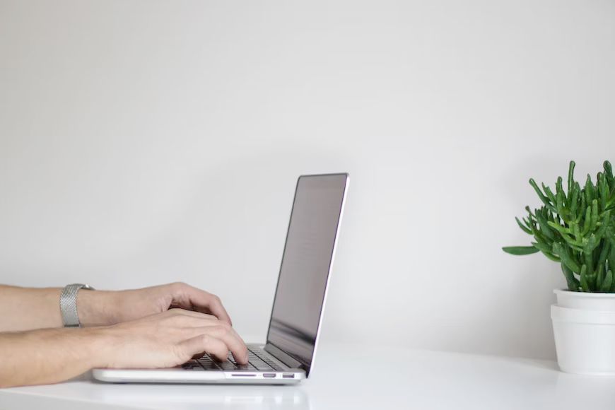 A person is typing on a laptop computer on a white table.