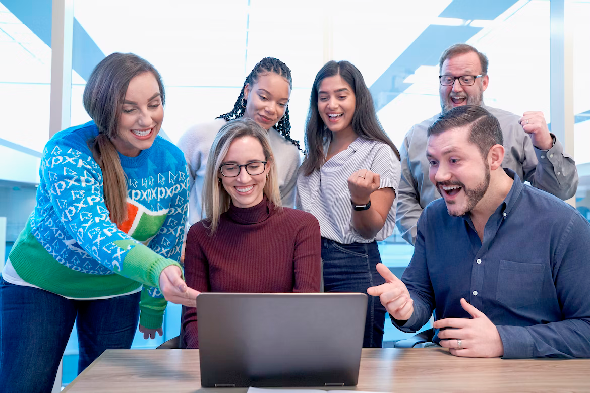 A group of people are standing around a laptop computer.