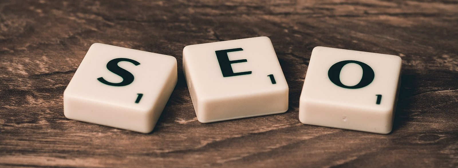 The word seo is written on scrabble tiles on a wooden table.