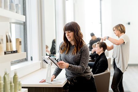 A woman is looking at a tablet in a hair salon.