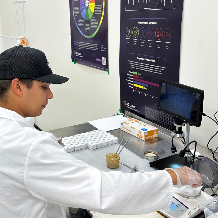 Person in lab coat working at a lab bench with a computer and microscope in a scientific workspace