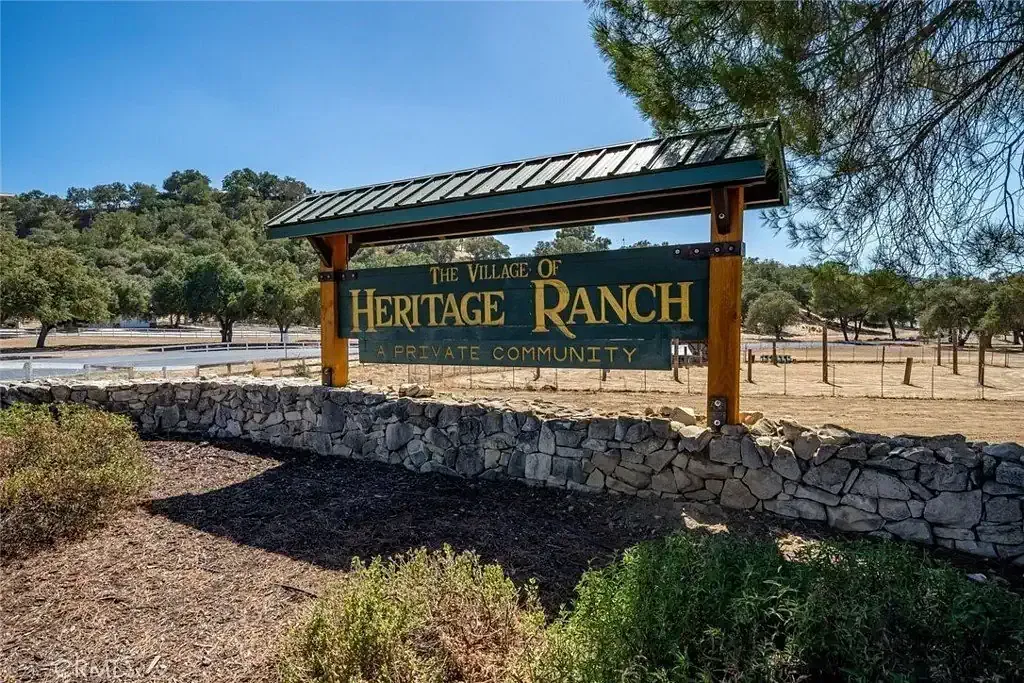 Entrada de Heritage Ranch, letrero verde y dorado junto a un camino de tierra y árboles.