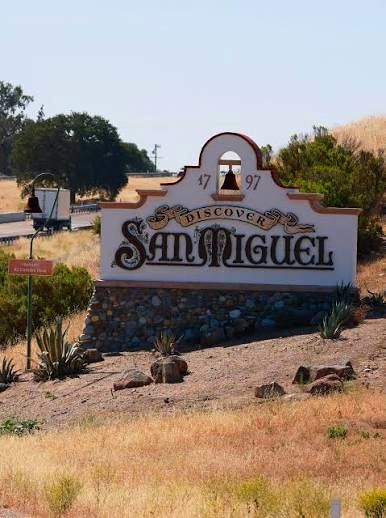 Welcome sign for San Miguel community with stone base and desert landscaping, under a clear blue sky